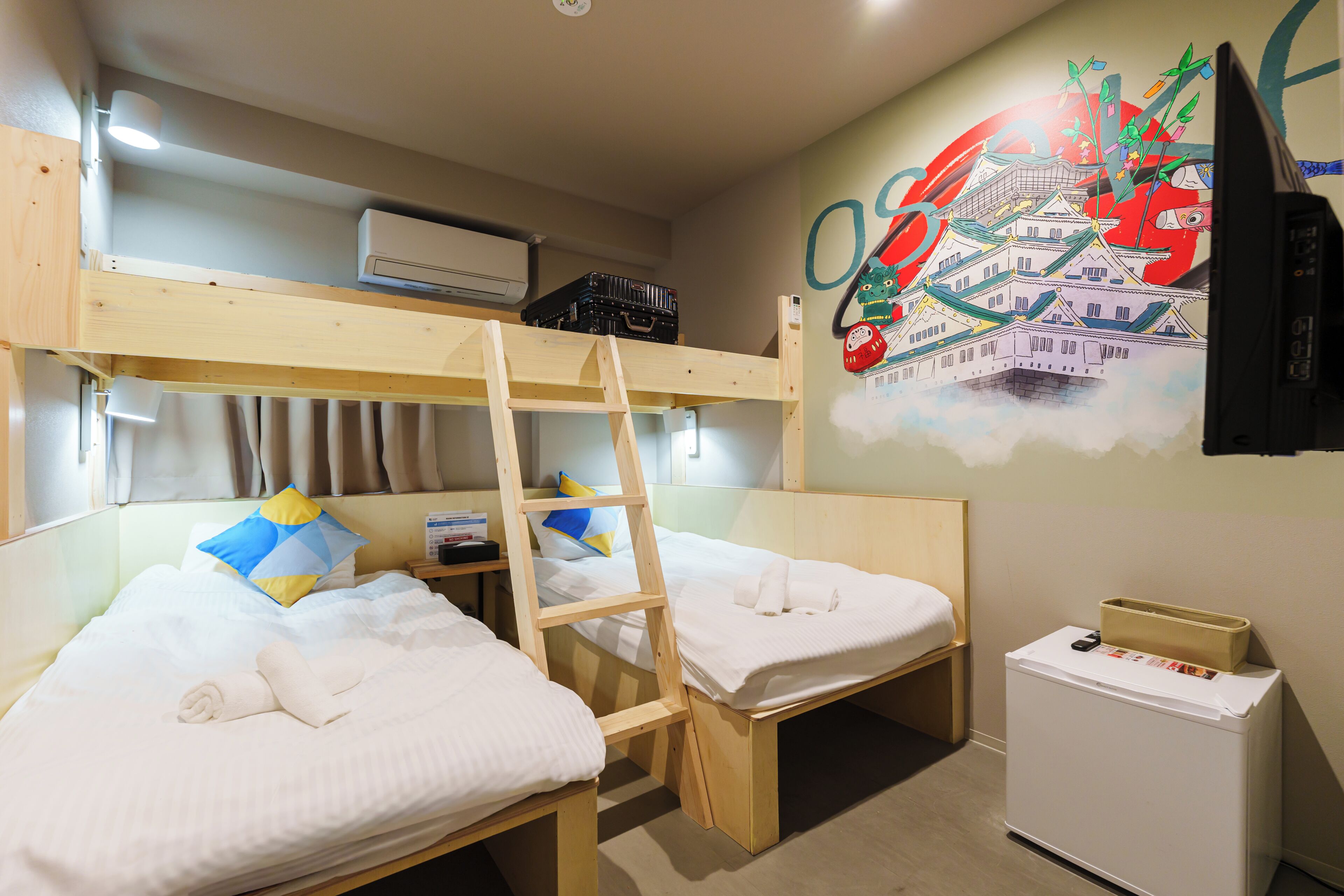 A bunk bed room with a ladder, a small refrigerator, and a wall with a colorful mural.