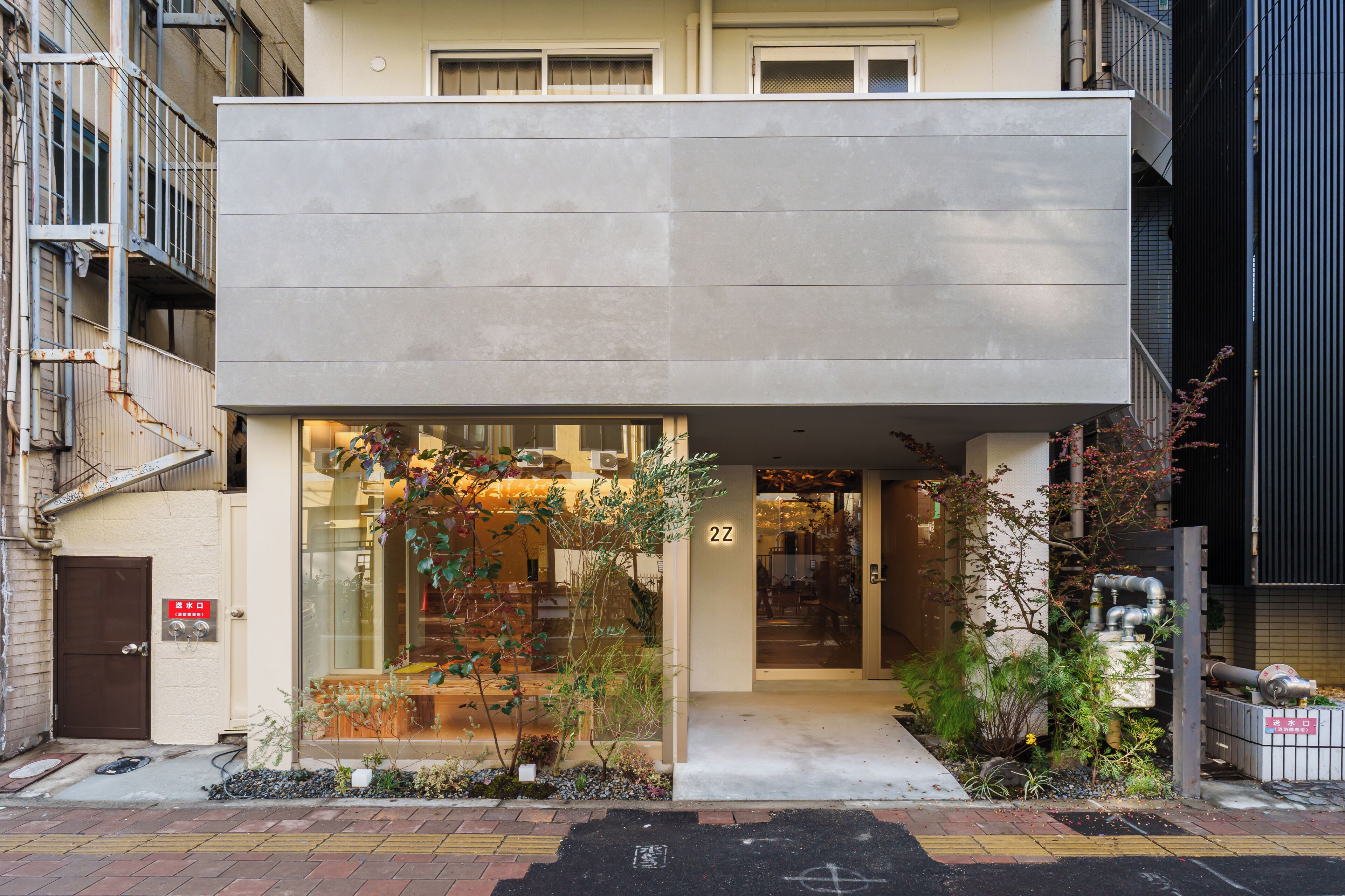 Un edificio moderno con ingresso a livello strada, il numero '2Z' ben visibile sulla porta e un piccolo giardino con piante.