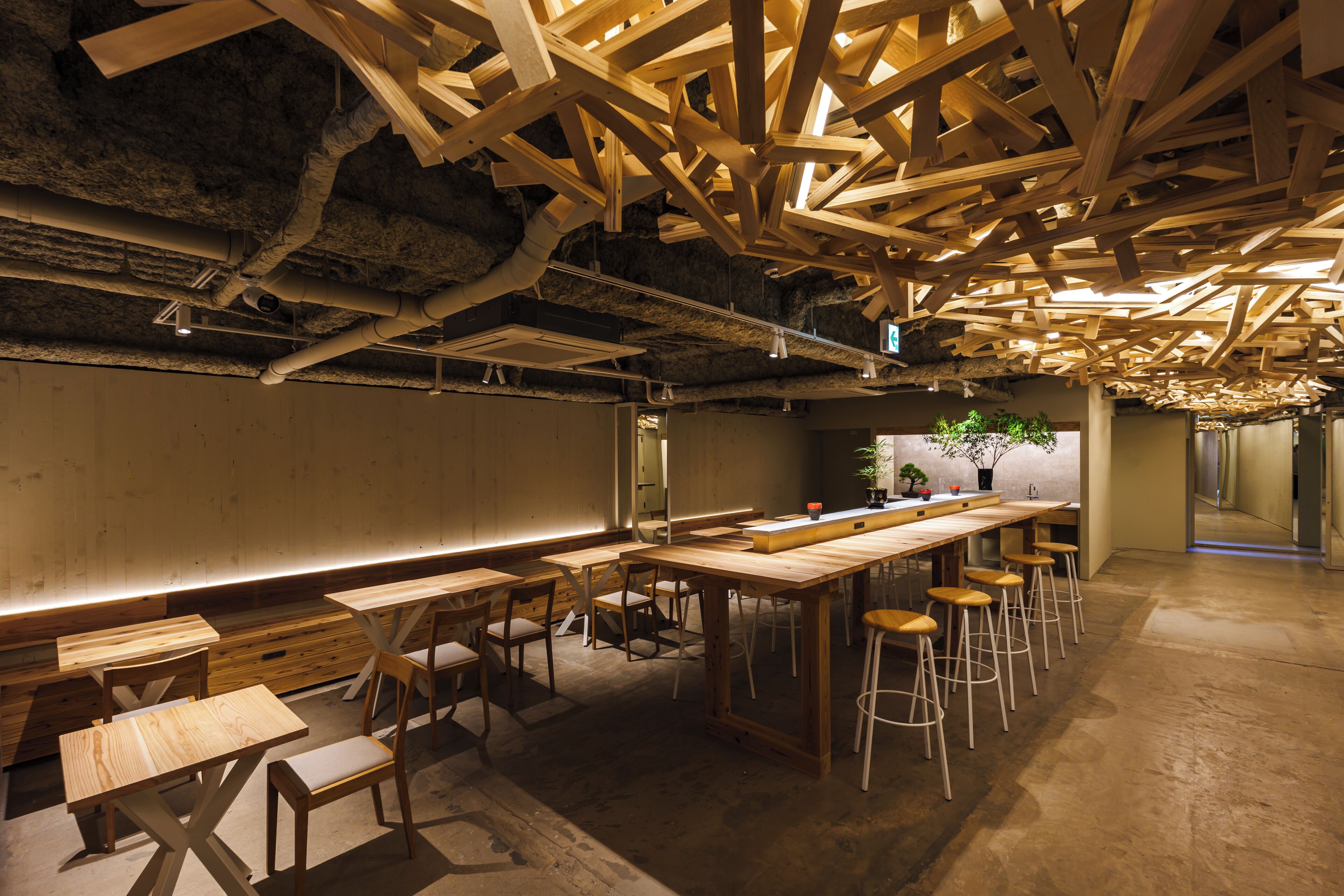 A modern interior with exposed wooden beams, a long bar area with stools, and a seating area with tables and chairs.