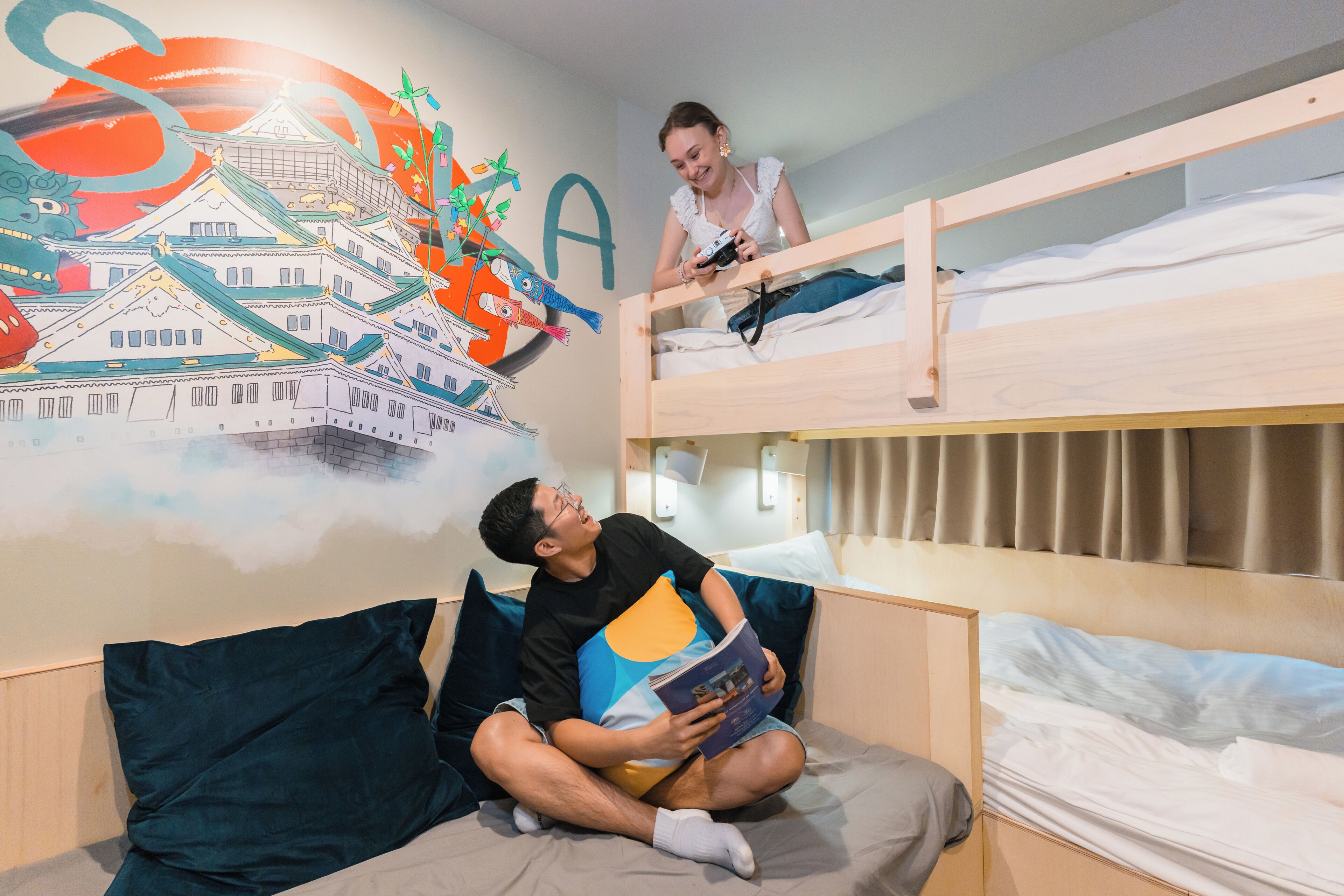 A bunk bed room with a mural, a person reading, and another person standing.