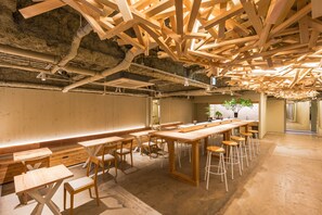 A spacious room with a high ceiling, wooden beams, and a long table with stools. - 2Z - DOYANEN HOTELS (Osaka)