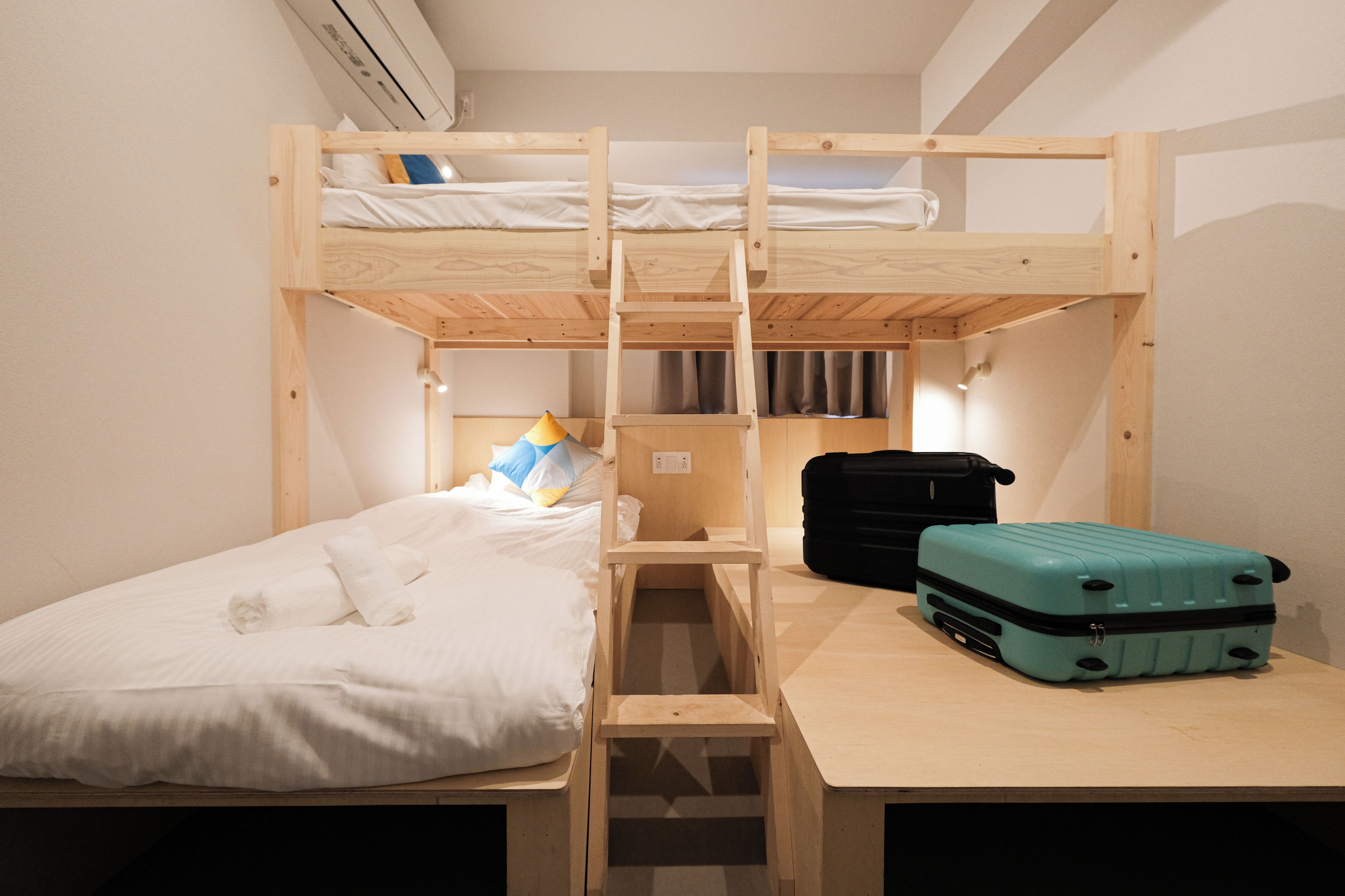 A bunk bed room with a desk, a suitcase, and a lamp.