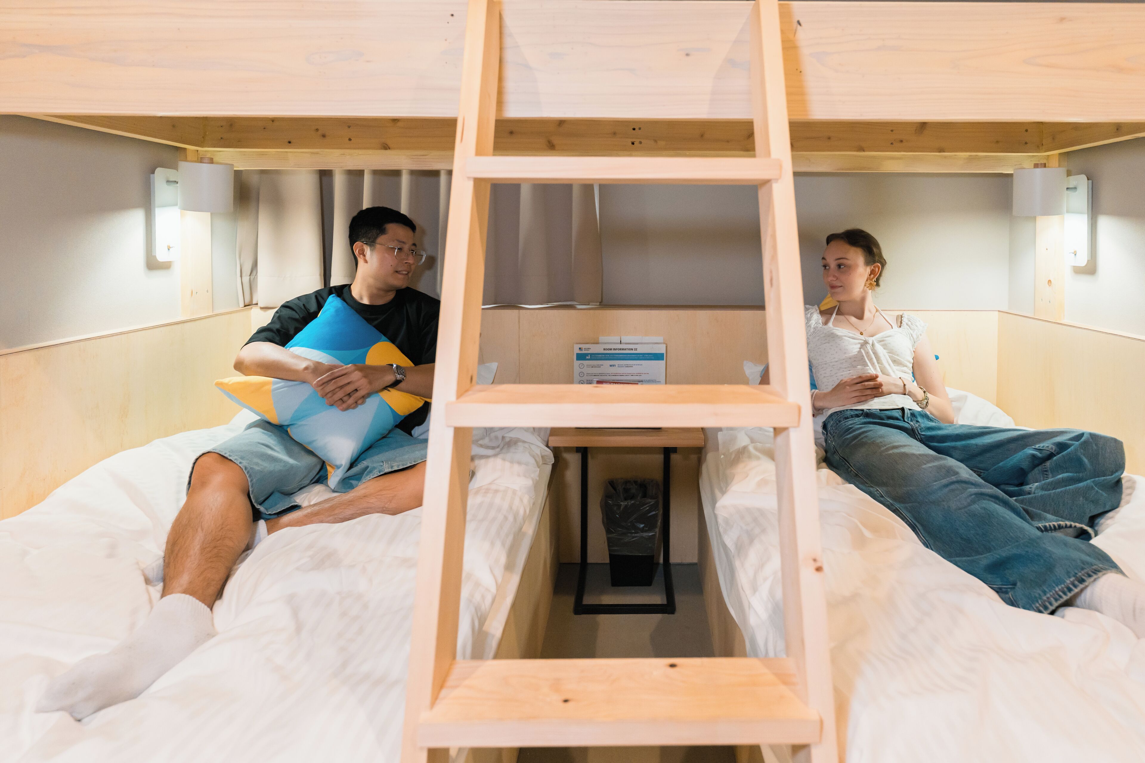 A bunk bed with a ladder, a small table, and a trash bin.