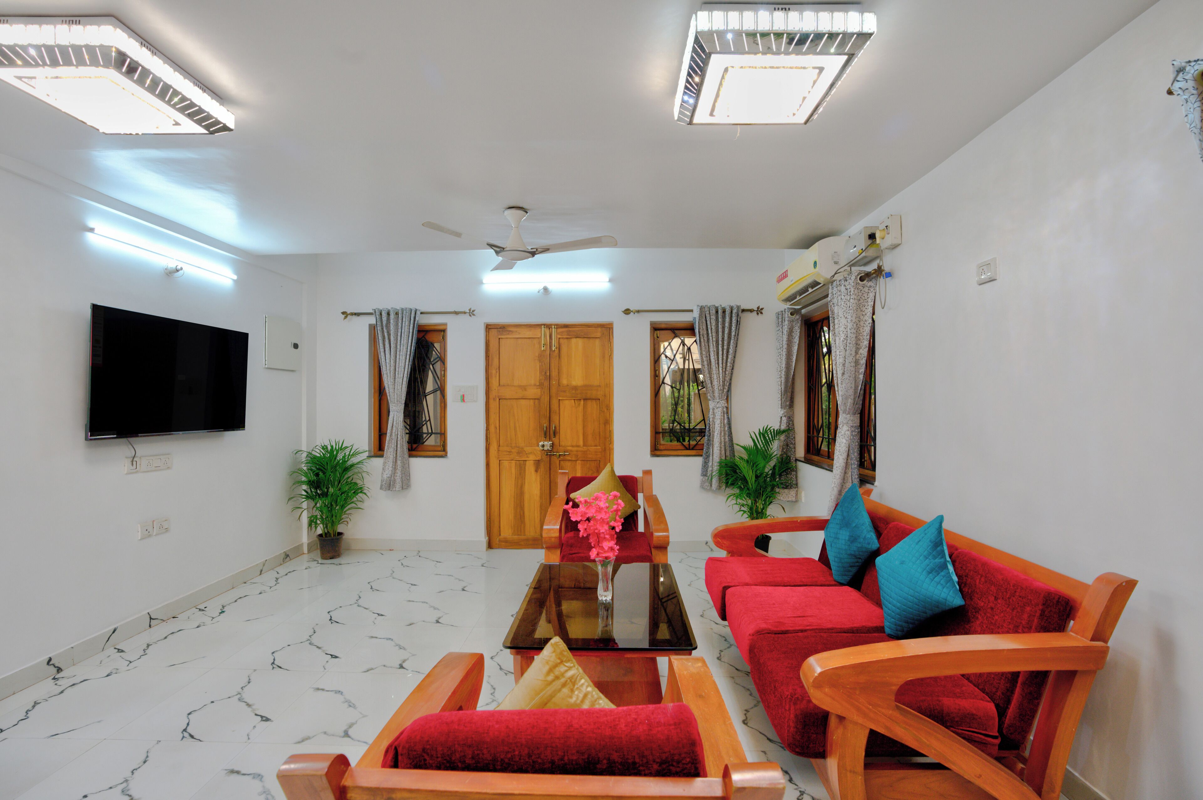 A living room with a flat-screen TV, red sofas, a wooden coffee table, and a ceiling fan.