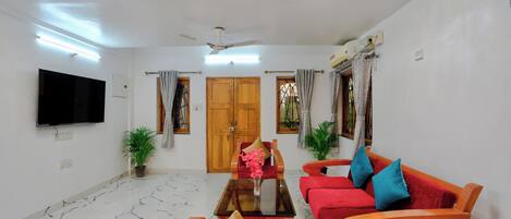 A living room with a flat-screen TV, red sofas, a wooden coffee table, and a ceiling fan.