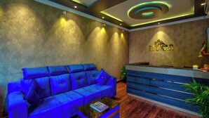 A reception area with a blue sofa, a reception desk, and a wall-mounted logo. - Hotel Eyokar Goa (Candolim)