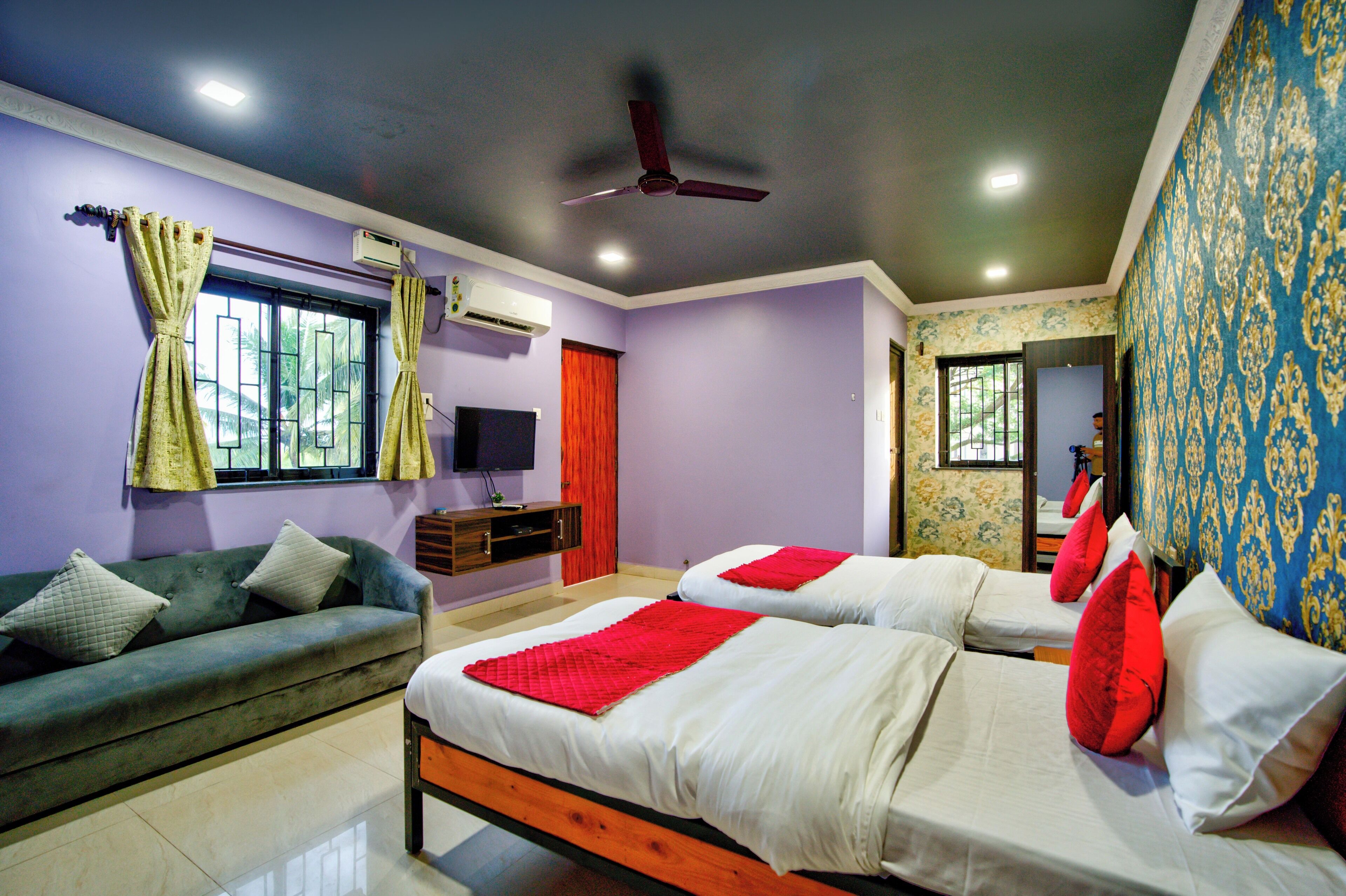 Habitación de hotel con dos camas, un sofá, un aire acondicionado, un ventilador de techo y un televisor.