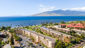 Un hotel costero con varias edificaciones, estacionamiento y vistas al océano y las montañas.
