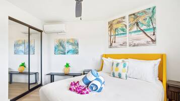 A hotel room with a bed, a ceiling fan, artwork on the walls, and a bench with a pineapple decoration.
