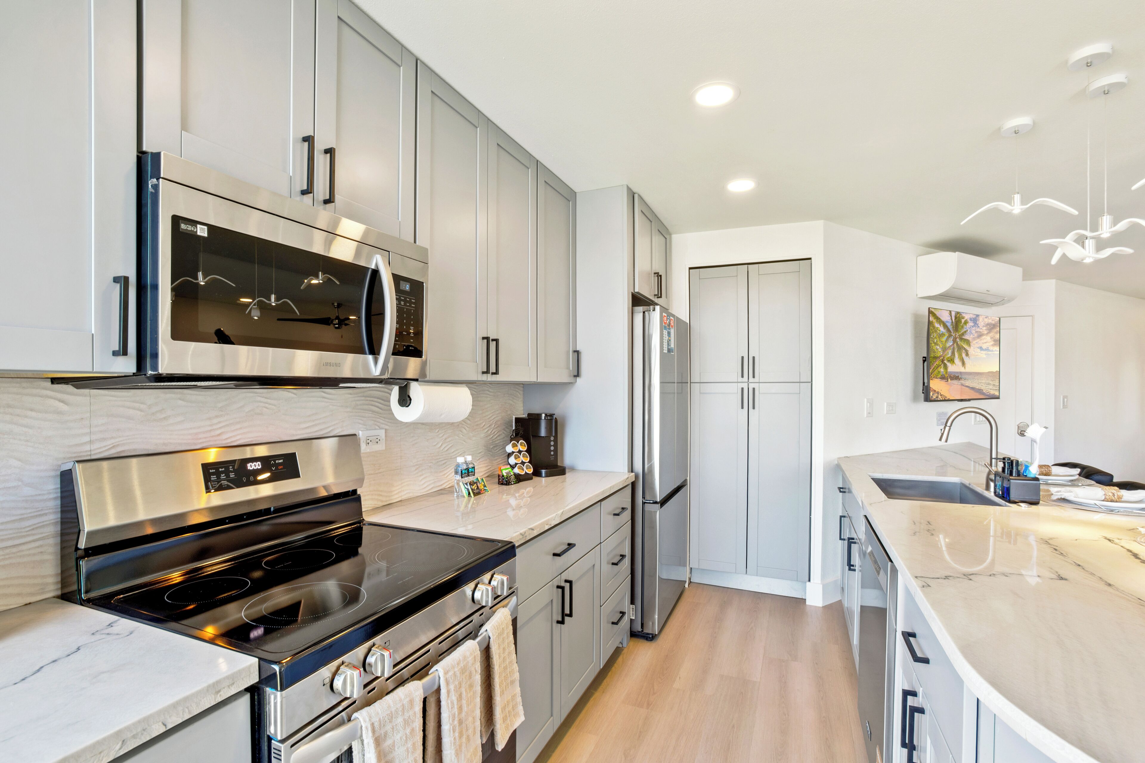 A modern kitchen with stainless steel appliances, grey cabinetry, and a marble countertop.