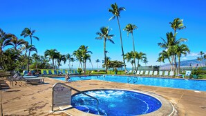 Un área de piscina con jacuzzi, palmeras y sillas de descanso.