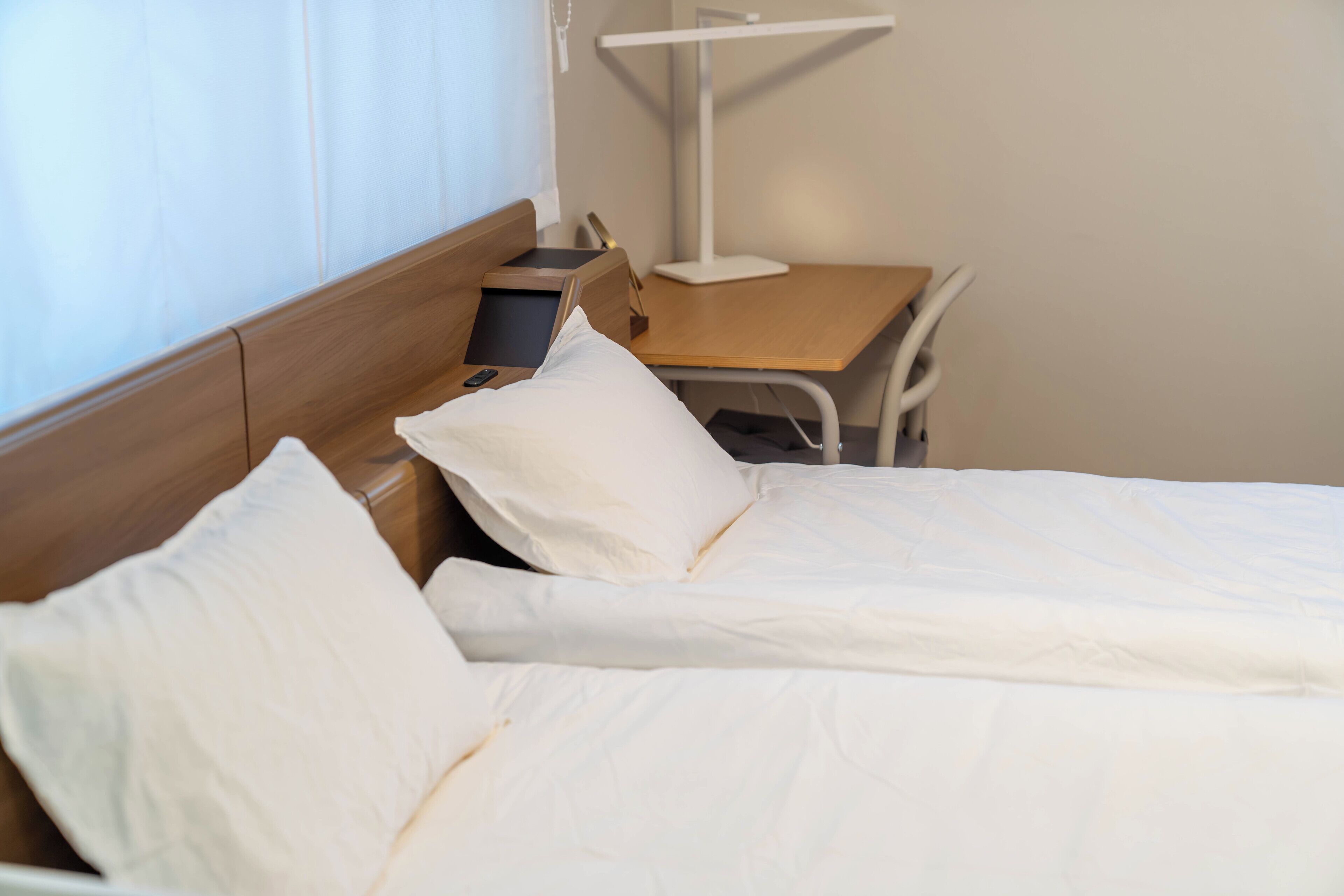 A hotel room with a bed, bedside table, lamp, and a chair.