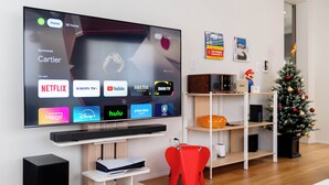 Ein modernes Wohnzimmer mit einem Flachbildfernseher, der verschiedene Streaming-Apps anzeigt, einer Weihnachtstanne und einer Spielkonsole.