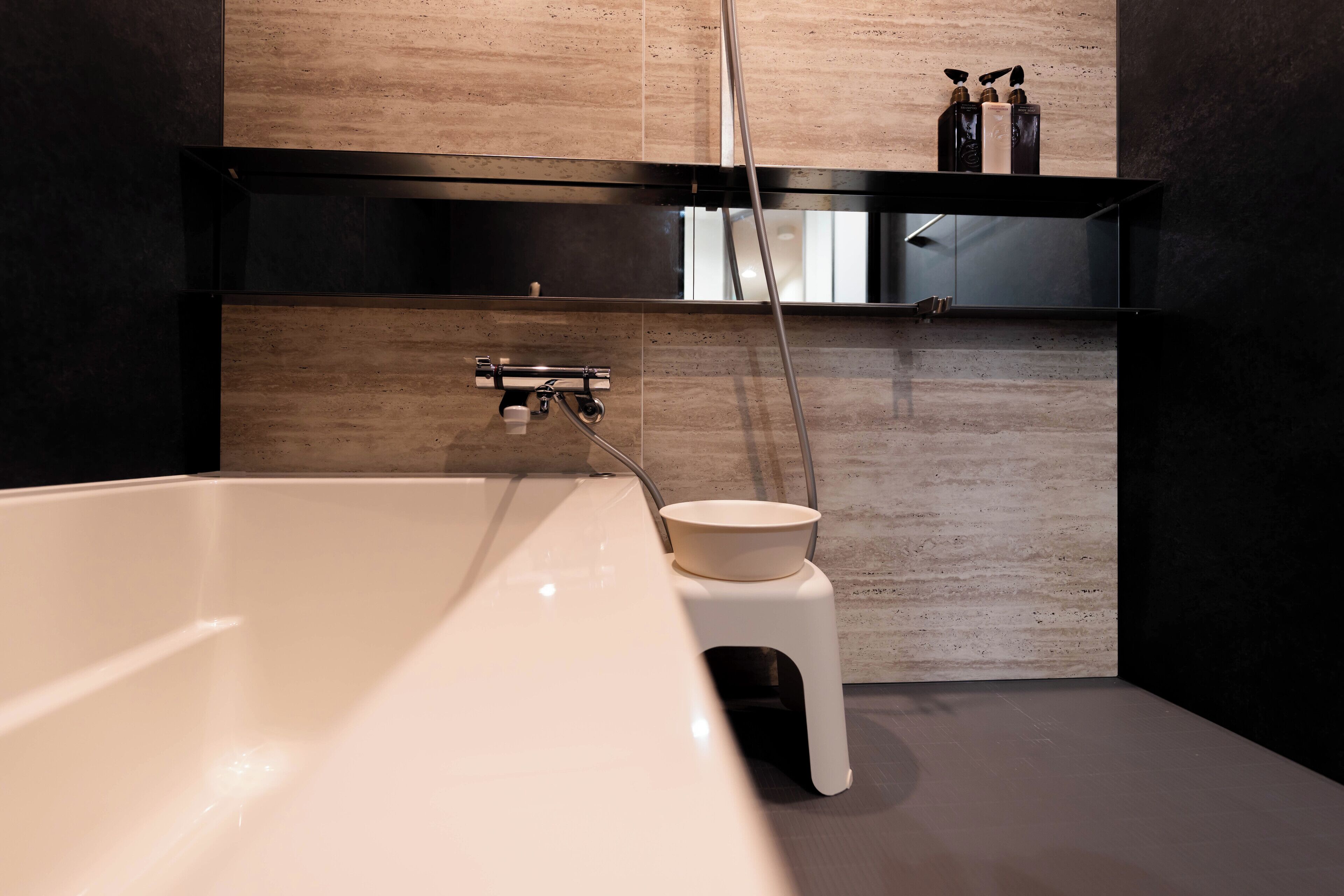 A modern bathroom with a large bathtub, a small stool, and a shelf with toiletries.