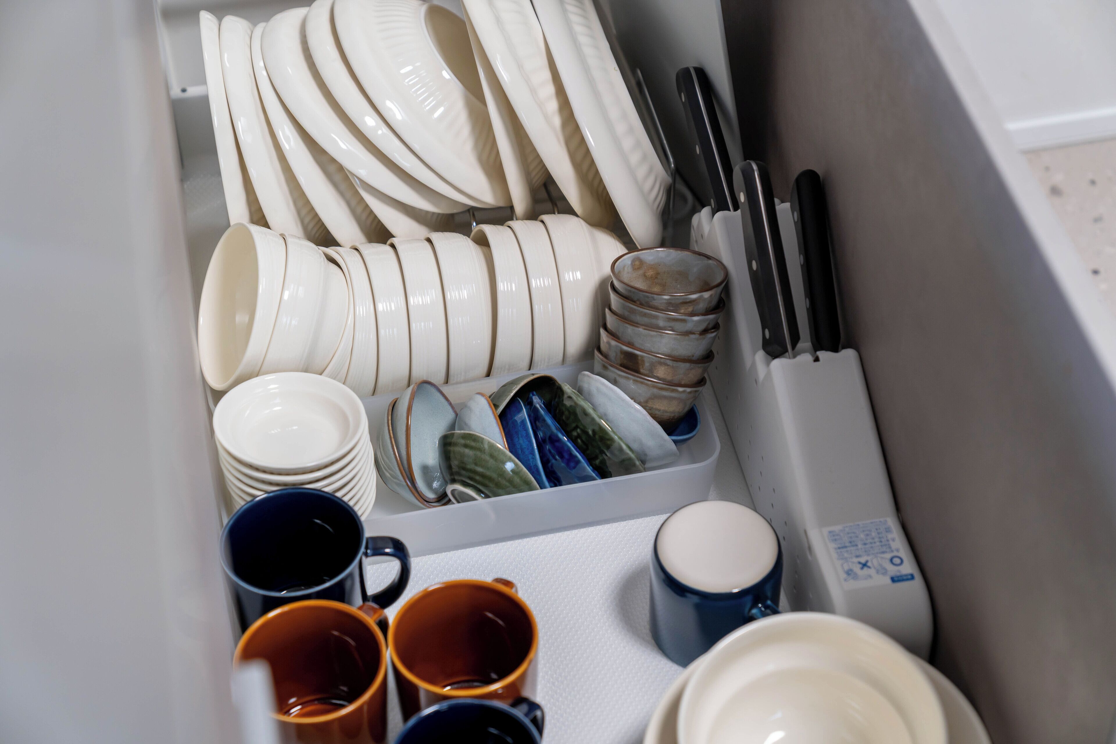 A kitchen drawer with neatly organized dishes, including plates, bowls, and mugs.