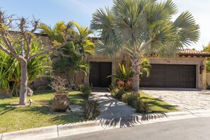 A residential property with a paved driveway, a garage, and various tropical plants. - Stunning 4BR Villa w/ Ocean Views, Infinity Pool, Hot Tub & Butler Service (Cabo San Lucas)