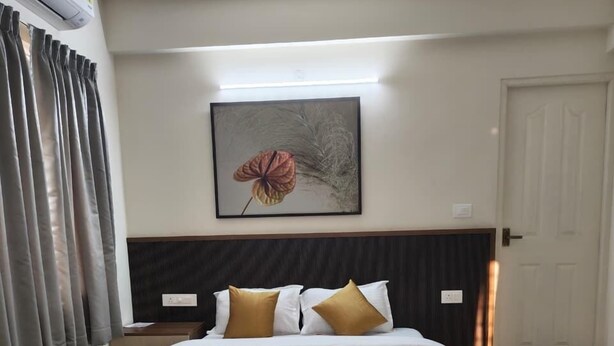 Een hotelkamer met een groot bed, hoofdeinde, een wandairconditioner, een lijstwerk en een deur.