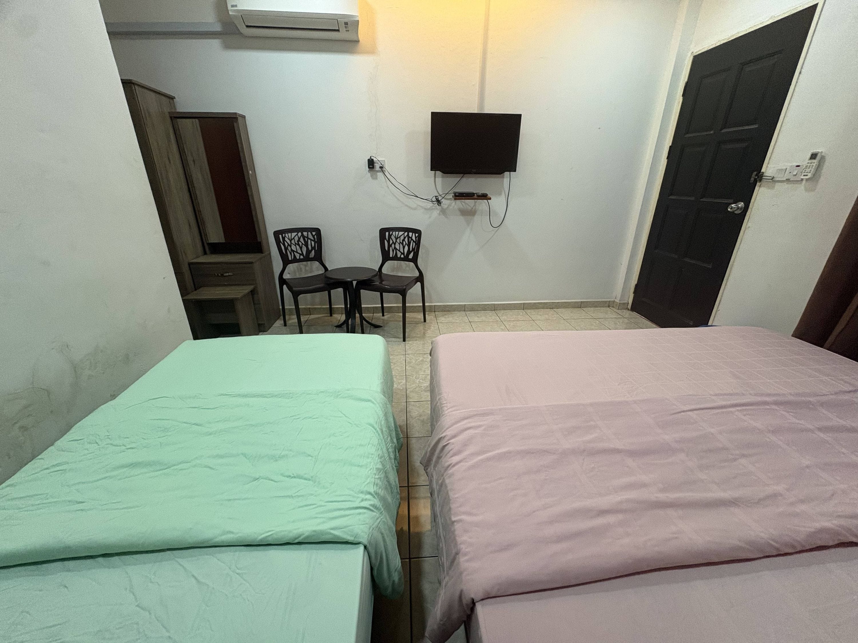 A room with two beds, a TV mounted on the wall, a small table with chairs, and a door.