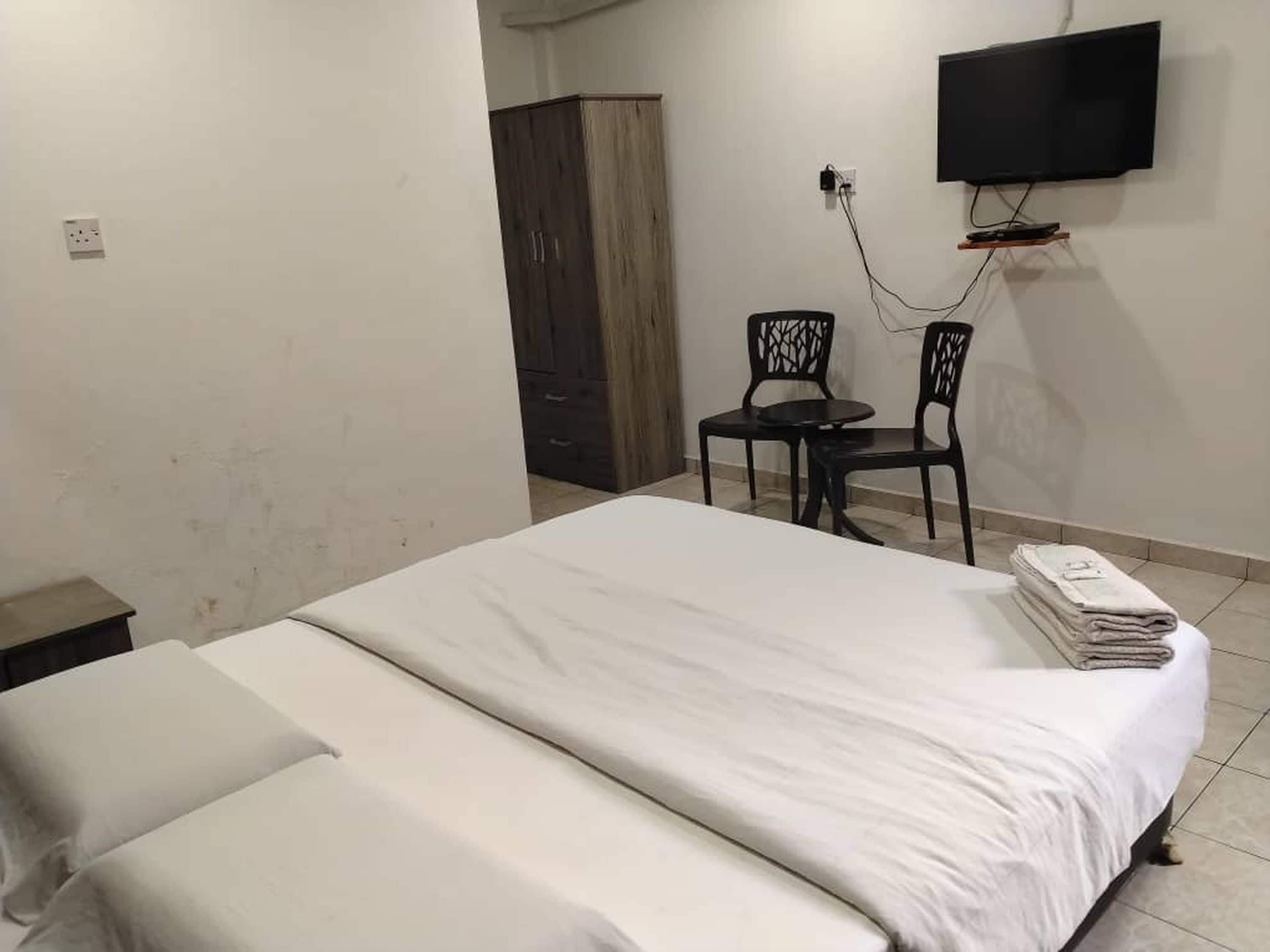 A hotel room with a bed, a desk with two chairs, a TV mounted on the wall, and a wardrobe.