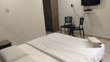 A hotel room with a bed, a desk with two chairs, a TV mounted on the wall, and a wardrobe.