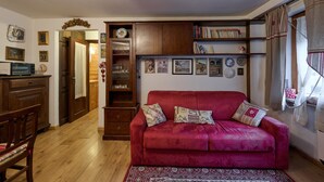 Un soggiorno con un divano rosso, mobili in legno e una libreria piena di libri e oggetti decorativi.