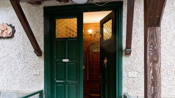 Una porta verde con una targa, una scala in pietra e un soffitto in legno.
