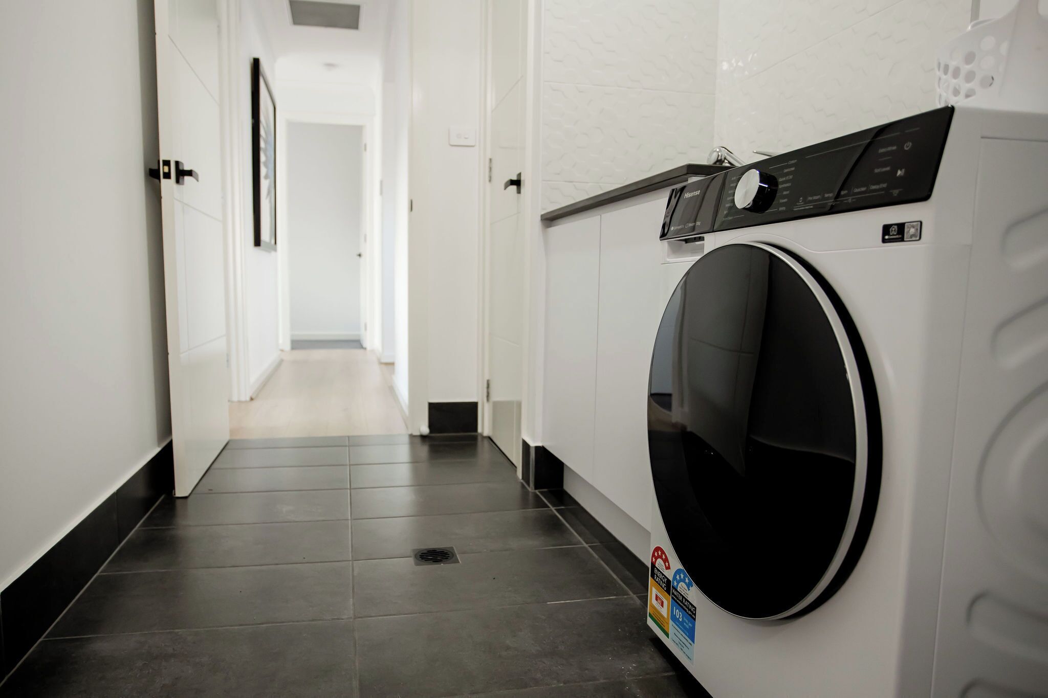 Een wasserette met een voorlader wasmachine, een bedieningspaneel en een betegelde vloer.