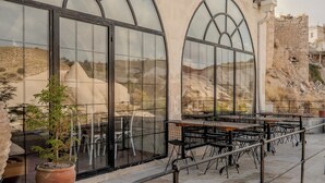 Μια βεράντα με καθιστικά σε εξωτερικό χώρο, μεγάλα τοξωτά παράθυρα και θέα σε ένα βραχώδες τοπίο.