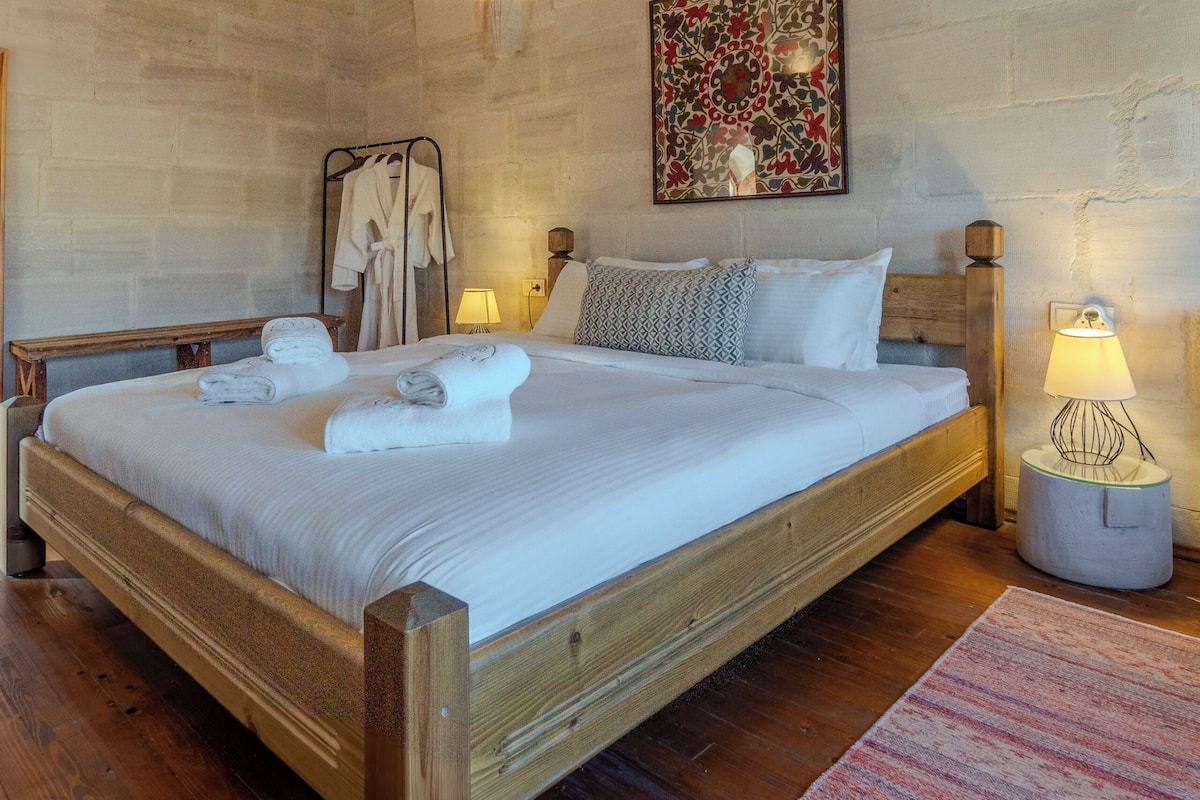 A spacious bedroom with a large bed, wooden headboard, and a stone wall.