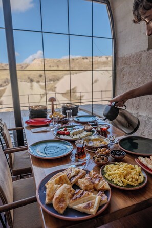 A dining table set with various dishes and a person pouring a drink. - Valinor Cappadocia (Urgup)