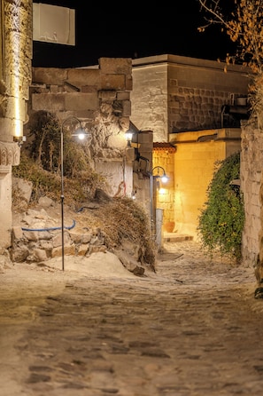 A narrow cobblestone street at night with stone buildings and street lamps. - Valinor Cappadocia (Urgup)