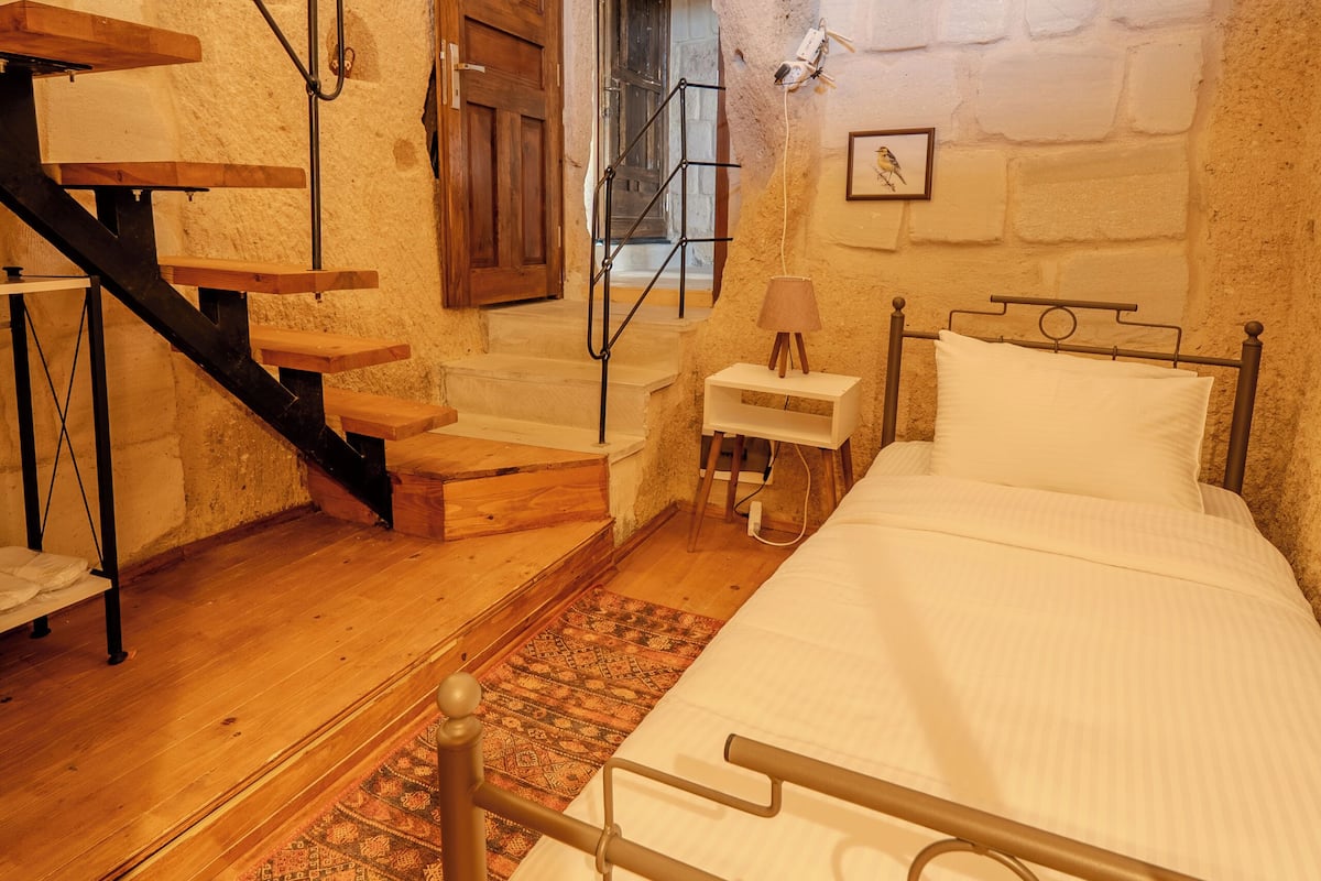 A bedroom with a bed, a nightstand, a lamp, a wooden staircase, and a patterned rug.
