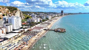Un paisaje urbano costero con una playa bordeada de sombrillas y un muelle que se adentra en el mar.