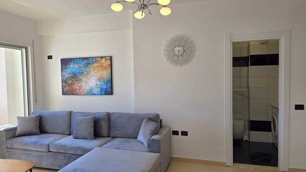 Una sala de estar moderna con un sofá seccional gris, un cuadro, un reloj de pared decorativo y vista al cuarto de lavado.