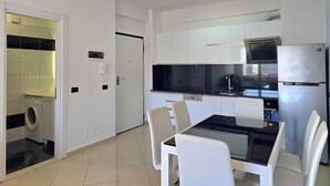 Una cocina moderna con armarios blancos, encimera negra y refrigerador de acero inoxidable.