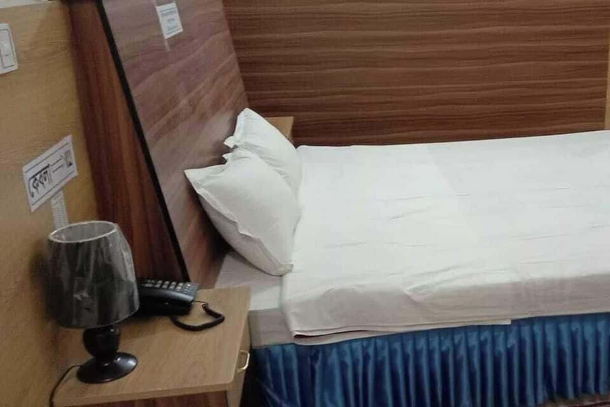 A neatly made bed with white linens, a blue skirt, and a lamp on a wooden nightstand.