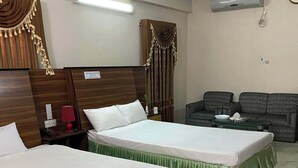 A hotel room with two single beds, a sofa, a nightstand with a lamp, and an air conditioning unit. - Hotel Castle Soad Bogura (Bogra)