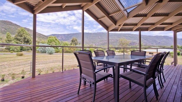 Eine überdachte Terrasse im Freien mit Tisch und Stühlen, mit Blick auf eine gebirgige Landschaft.