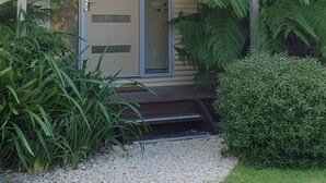 Ein Haus mit überdachter Veranda, einer Haustür und einem kleinen Vorgarten mit Pflanzen und Kies.