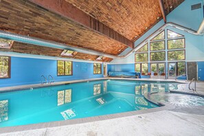 Une grande piscine intérieure dotée d’un plafond en bois, de grandes fenêtres et d’un espace sauna.
