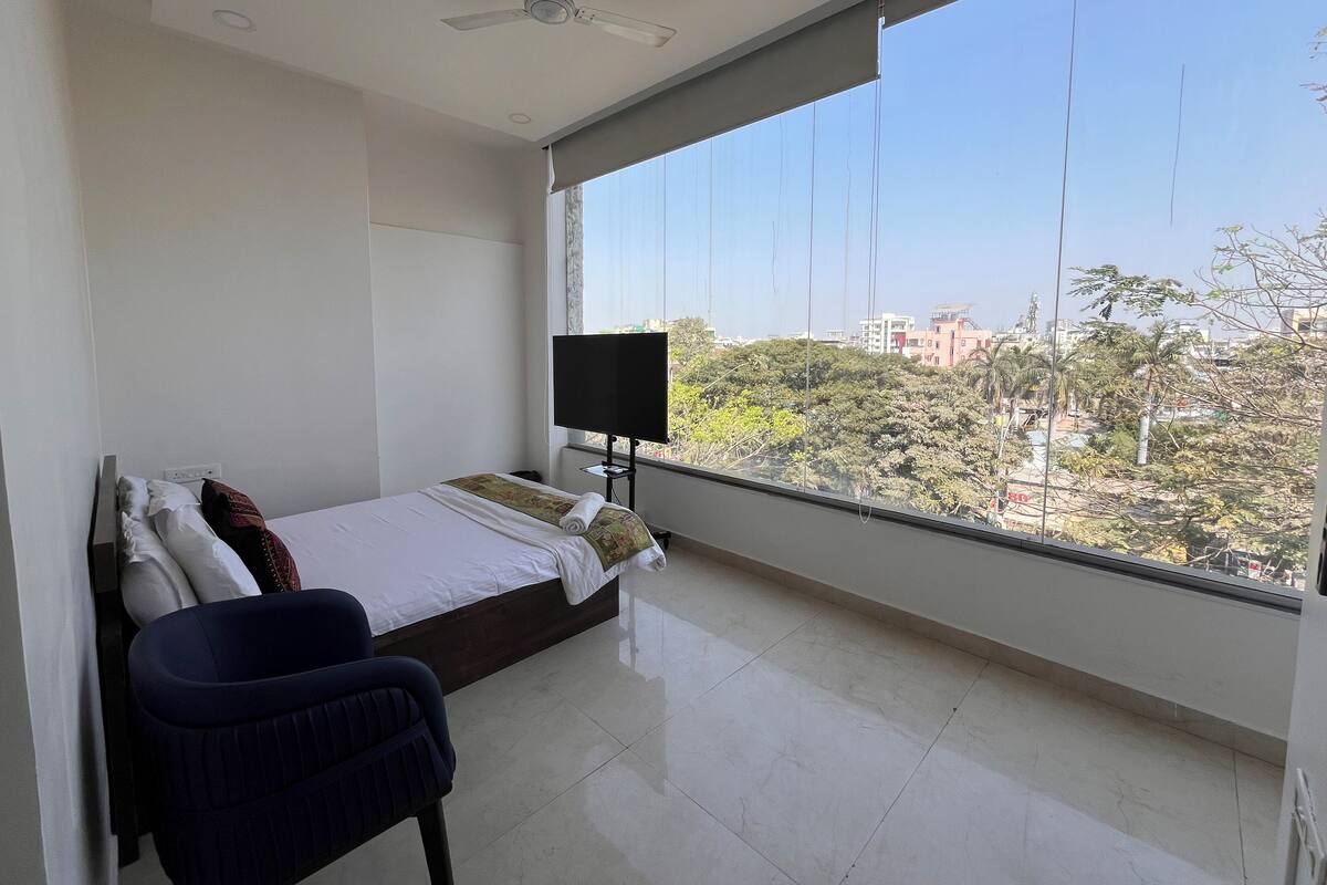 Una camera da letto con un letto, una televisione, una sedia e un'ampia finestra vista città.