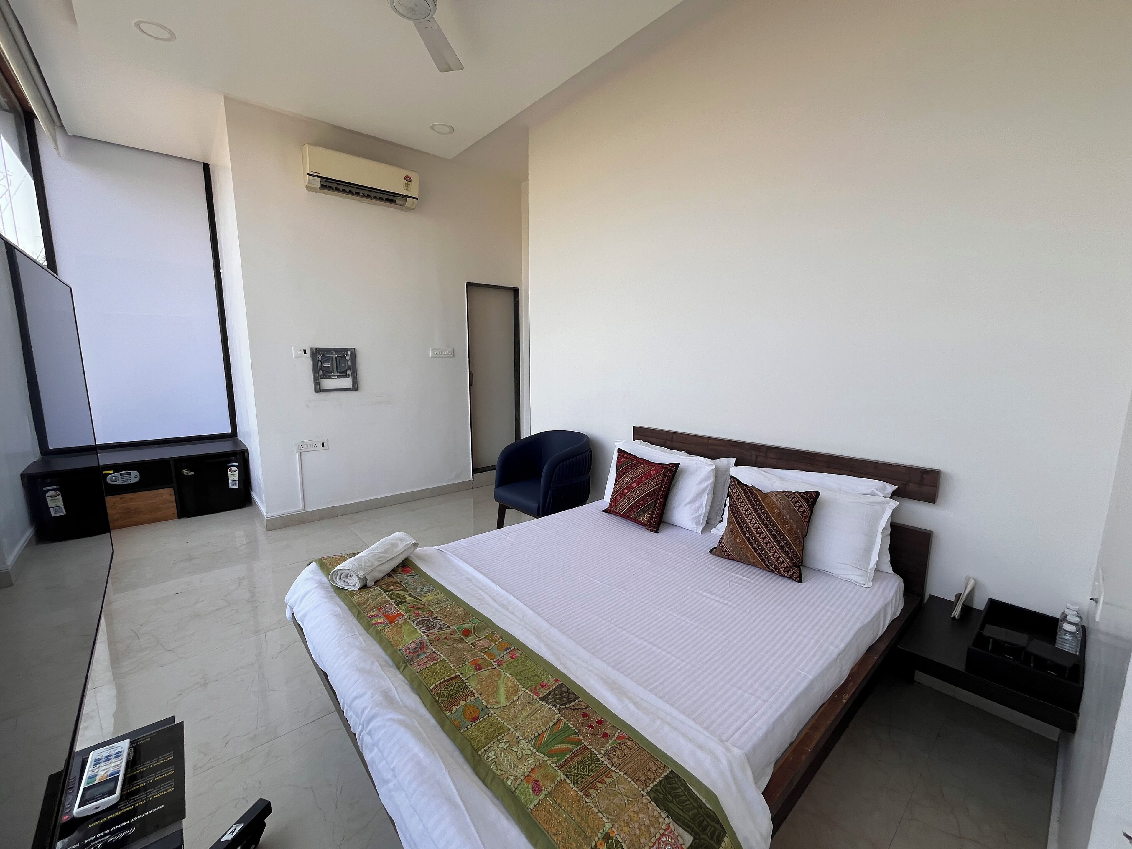 A hotel room with a large bed, a desk with a chair, an air conditioning unit, and a television.