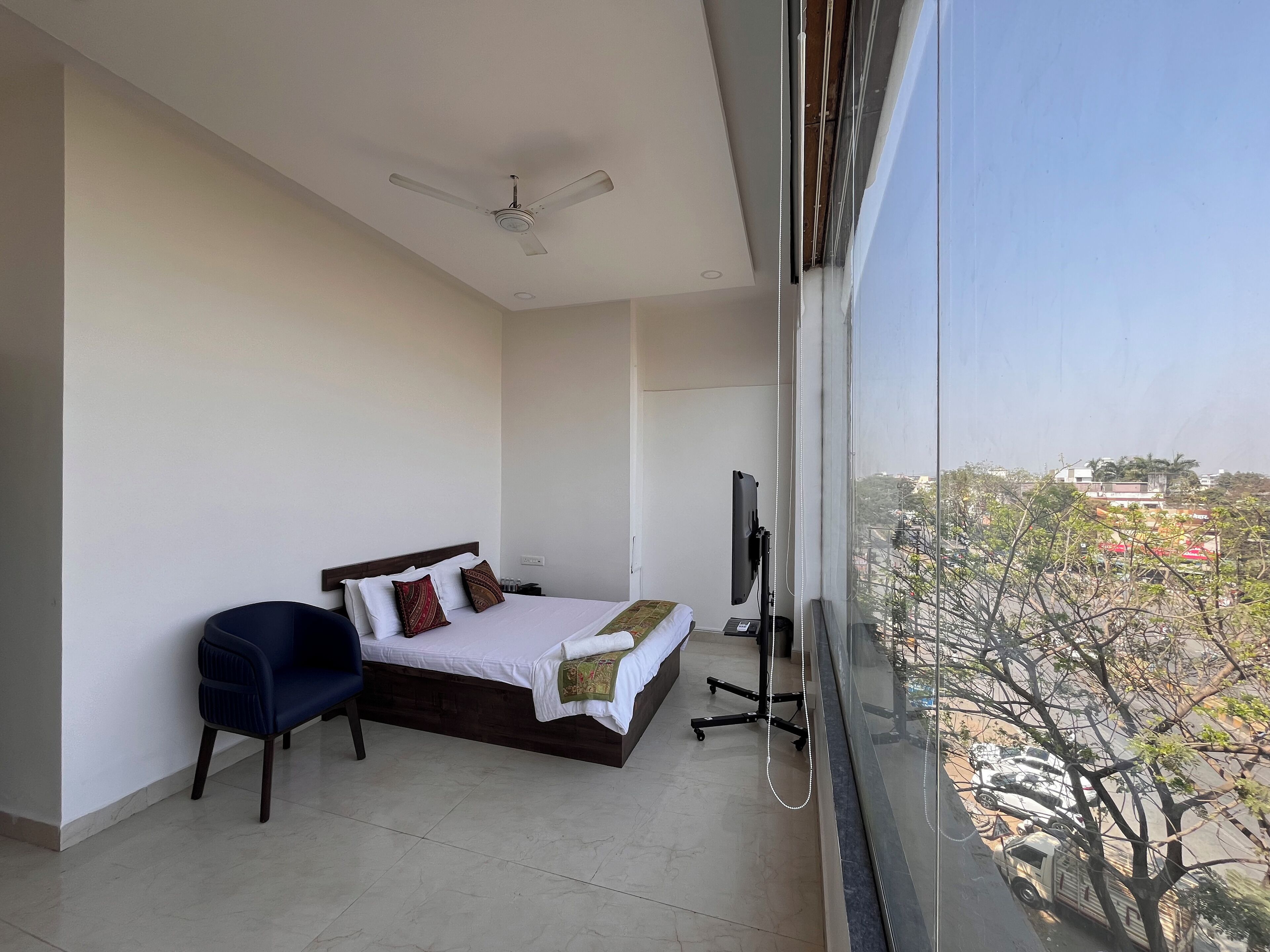 A bedroom with a bed, a chair, a TV, and a ceiling fan.