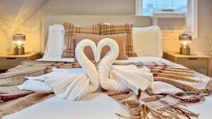A neatly made bed with a heart-shaped towel arrangement, a plaid blanket, and a city view through the window. - Sweet 4BR Steps from UW | Prime Location @Seattle (Seattle)