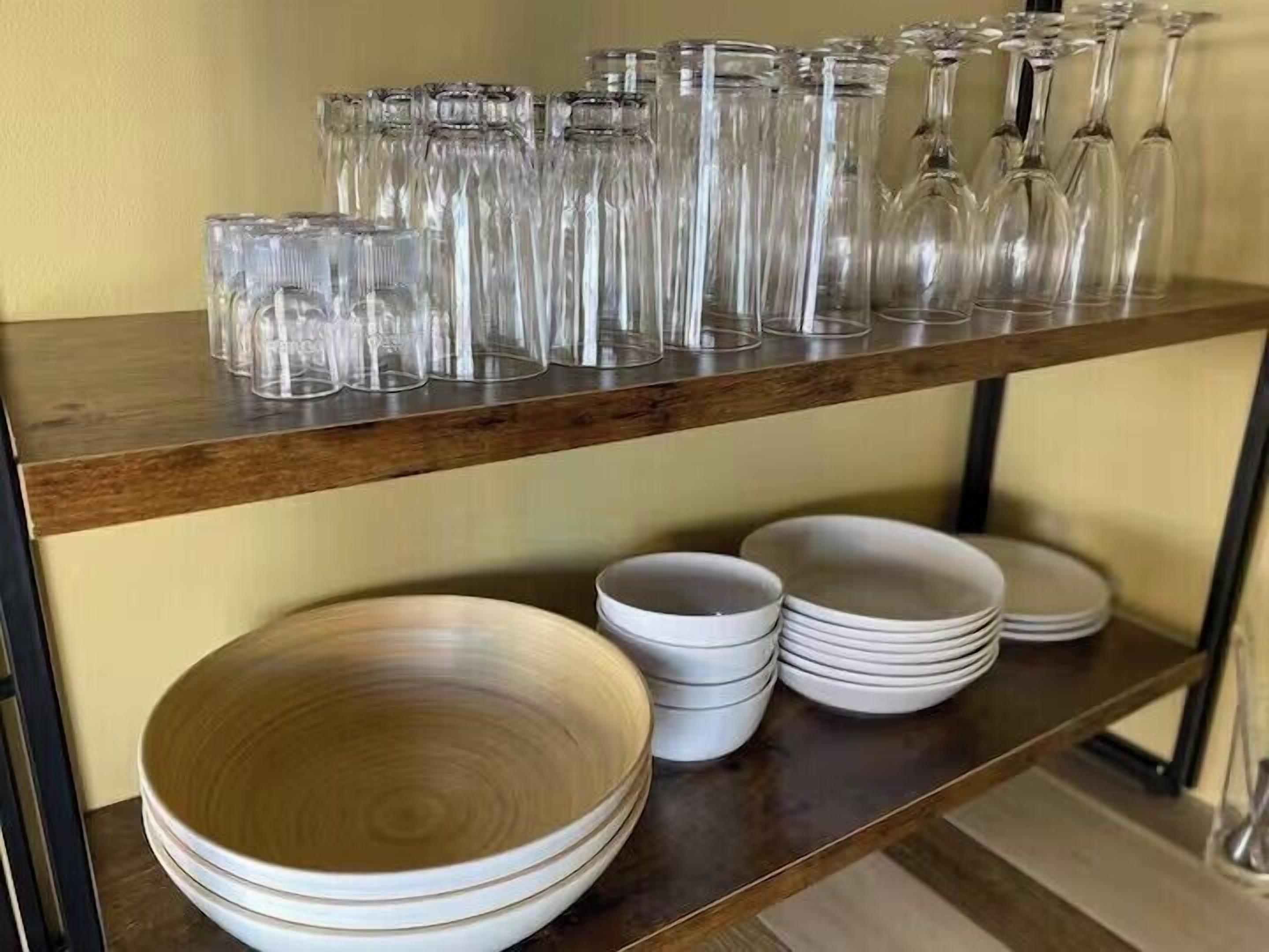 A wooden shelf with clear glassware and stacked white plates.