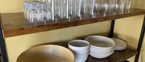 A wooden shelf with clear glassware and stacked white plates.
