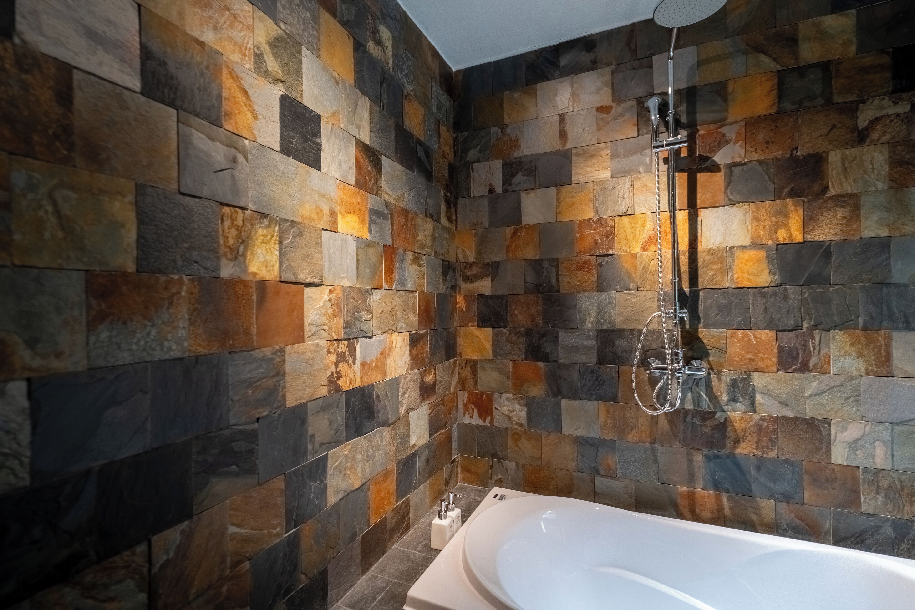 A modern bathroom with a stone mosaic wall, a freestanding bathtub, and a handheld showerhead.