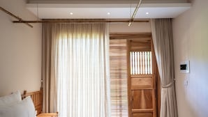 Een slaapkamer met een bed, gordijnen, een houten deur en een plafondlamp.