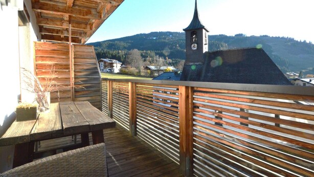 Una terraza de madera con vistas a una torre del reloj y montañas al fondo.
