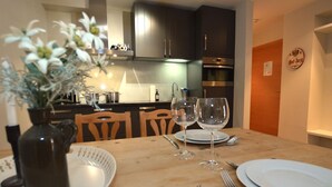 Una mesa de comedor lista con platos, copas de vino y cubiertos. Hay un florero con flores sobre la mesa.